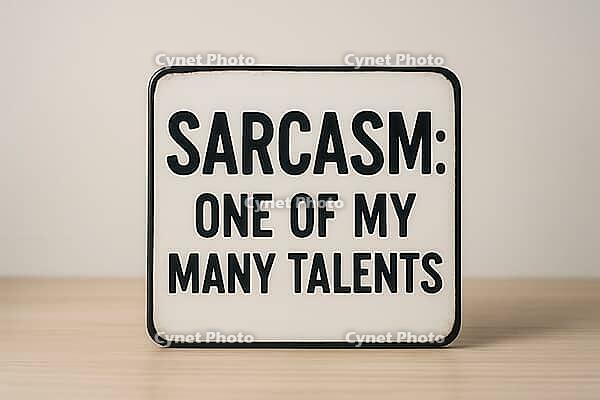 White sign with black writing placed on a wooden table, displaying the funny quote sarcasm, one of my many talents, AI generated [IBR125421239]