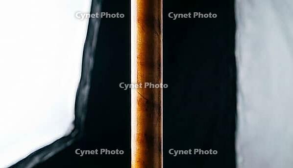 Close-up of a single deep amber aramid fiber under tension in vertical orientation, dark background, ballistic materials science macro photography, AI generated [IBR125421274]
