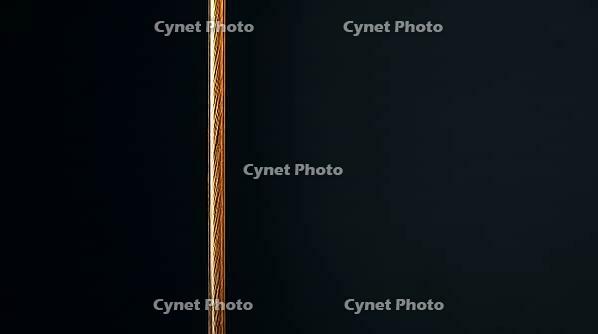 Close-up of a single deep amber aramid fiber under tension in vertical orientation, dark background, ballistic materials science macro photography, AI generated [IBR125421277]
