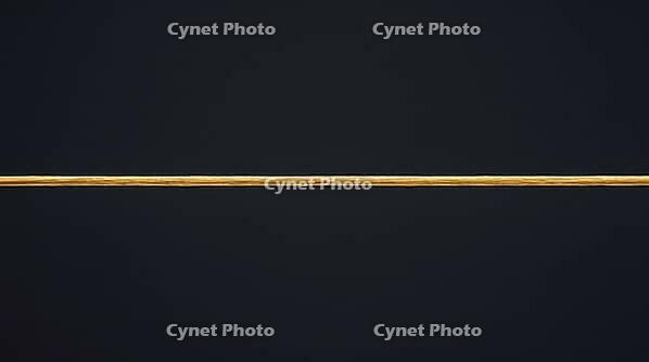 Close-up of a single taut golden yellow aramid fiber under tension with fine longitudinal striations, dark background, ballistic materials science macro photography, AI generated [IBR125421281]
