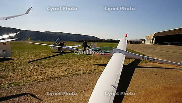 People working on gliders in an open field near a hangar under a bright sky, Aérodrome de Château-Arnoux - Saint-Auban, France [IBR125421618]