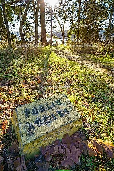 A public access sign along a sunlit forest path, surrounded by trees and fallen leaves, creating a tranquil natural setting. A marker denoting public access next to a walking path, Gabriola Island, British Columbia, Canada [IBR125421633]