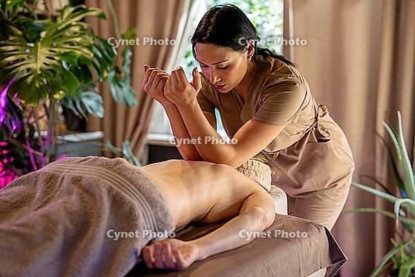 Professional masseuse making special relaxing back massage for woman client using hands, female on spa bed receiving massage treatment, beauty procedures and regular body care for healthy living [IBR125421684]
