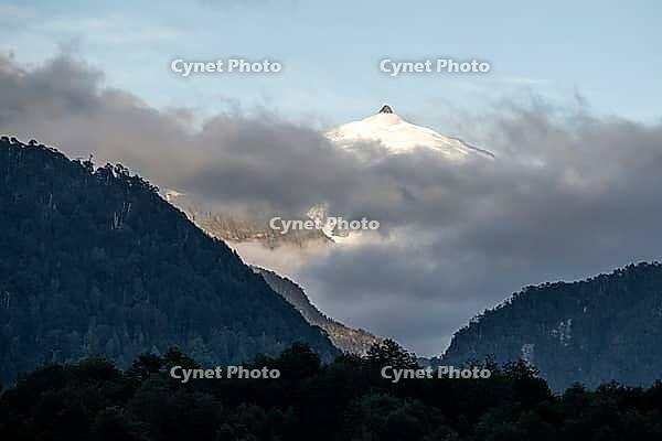 Glaciated impressive mountain peak, mountains with forest, last clouds of fog moving around in the morning, Carretera Austral, near Villa Santa Lucia, Los Lagos, Chile [IBR125423492]