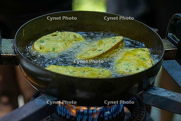 Golden brown fritters sizzle and bubble as they cook in a dark metal pan filled with bubbling hot oil over a blue gas flame, Bridal Falls, Rosedale BC Canada [IBR125424485]
