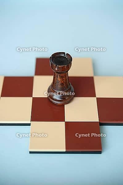 A dark wooden rook on a brown and beige chessboard with a light blue background [IBR125424498]