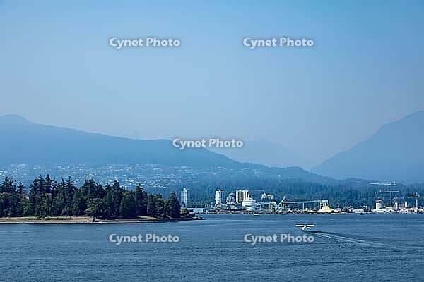 A small seaplane departs from the calm waters of Vancouver's harbor, with forested Stanley Park and distant mountains forming a scenic backdrop, Canada place, North Vancouver, BC Canada [IBR125424523]
