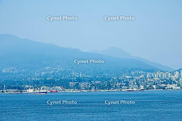 A wide view of the Vancouver skyline with lush green mountains in the background and ships sailing on the ocean, Canada place, North Vancouver, BC Canada [IBR125424533]