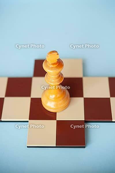 A yellow wooden king on a brown and beige chessboard against a light blue background [IBR125424559]