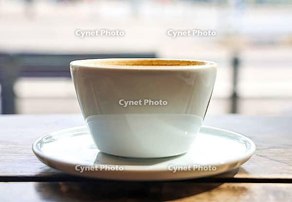 Coffee cup with crema on a saucer, illuminated by natural light through a cafe window [IBR125424565]