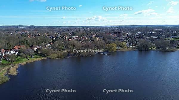 Aerial view showing village houses on the shore of a dark blue lake under a bright sky [IBR125436242]