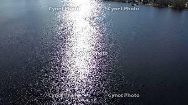 Sun reflecting on a lake surface creating a path of shimmering light, with land visible in the distance [IBR125436276]