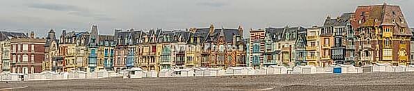 The Belle epoque and Art Nouveau in the seaside resort of Mers-les-Bains. Beach cabins sit on pebbles by the shore. Colorful buildings rise. Mers-les-Bains, Somme, France [IBR125436305]