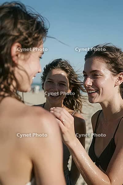 Authentic female bonding under bright sunlight, young women enjoying summer holiday warmth, tactile connection celebrating radiant youthful vitality, gentle touch on sun kissed skin as an embodiment of empathetic care, mutual affection, carefree seaside a [IBR125446414]