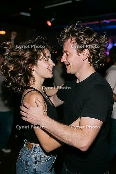 Authentic young couple dancing with joyful intimacy on a vibrant nightclub floor, dynamic motion of wavy brunette hair and shared affectionate smiles, the close embrace and tender eye contact manifest profound romantic chemistry amidst energetic club cult [IBR125446417]