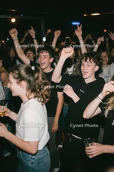 Youthful euphoria and collective effervescence among dancing teenagers in an energetic nightlife setting, emotional liberation and vibrant celebration, raised fists and victorious gestures manifest uninhibited joy, dynamic clubbing atmosphere intertwines  [IBR125446420]
