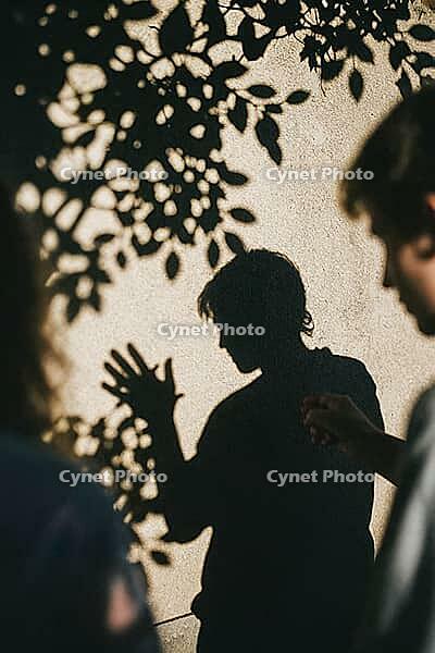 Shadow play and expressive hand gestures on textured stucco reflect nonverbal communication, emotional nuance, interpersonal resonance and internal dialogue, high contrast sunlight projects botanical foliage patterns above an introspective silhouette evok [IBR125446423]