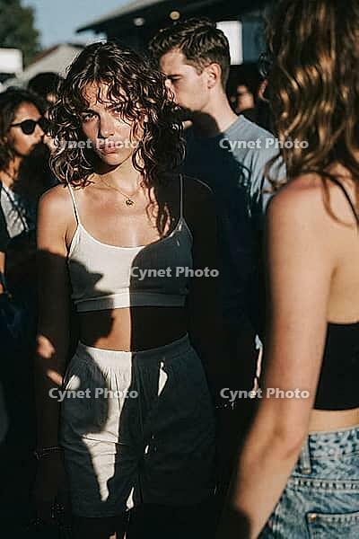 Youthful detachment and introspective solitude amid a crowded festival crowd, direct gaze conveying emotional vulnerability, shadow patterns slice across the body as an existential barrier, an evocative metaphor for inner alienation within bustling social [IBR125446425]