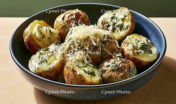 Freshly baked potatoes with melted cheese and green herbs in a ceramic bowl, AI generated [IBR125446429]