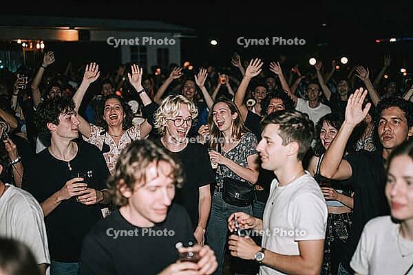 Ecstatic youth subculture embracing nocturnal open air concert freedom, joyful friends raising hands in celebration, nocturnal festival escapism, laughing partygoers holding drinks while swaying to rhythmic acoustic vibrations, emotional social bonding un [IBR125446433]