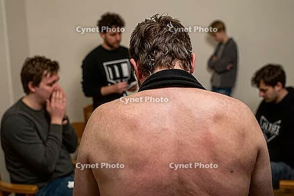 Vulnerable shirtless man surrounded by supportive peers in emotional group therapy session experiencing anxiety tension vulnerability and catharsis, raw human exposure manifests through physical posture and bare shoulders confronting unresolved collective [IBR125446436]
