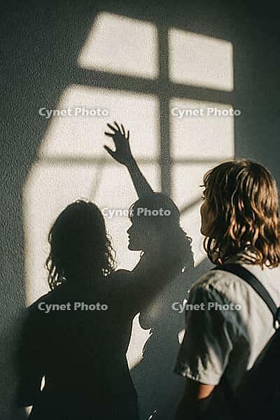 Silhouetted hand reaching toward window light cast on concrete wall, intimate human connection, longing, shadow play, emotional duality, introspective youth, artistic framing through natural sunlight, contrasting contours of two figures projecting their i [IBR125446441]