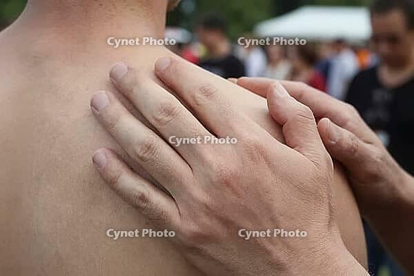 Hands resting gently on a bare shoulder convey deep empathy, comfort, solidarity, reassurance and physical connection during an open air gathering, tactile interaction offering solace amidst a crowded public environment, interpersonal care bridging emotio [IBR125446452]