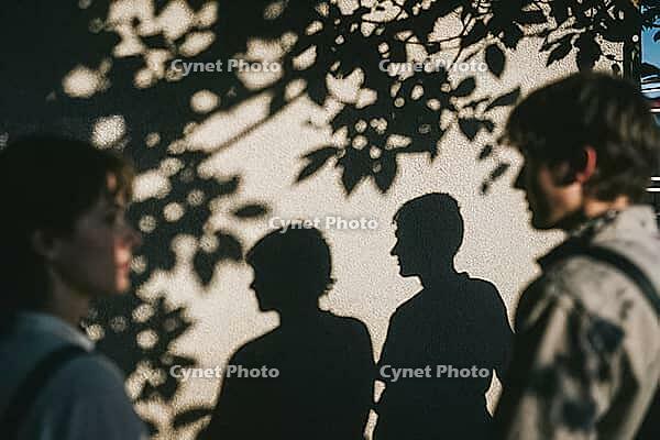 Interpersonal resonance and emotional projection, young people standing opposite each other while their dark silhouettes cast an intimate dialogue upon a bright stucco facade, dappled foliage contours intertwining with human profiles, subconscious nonverb [IBR125446457]