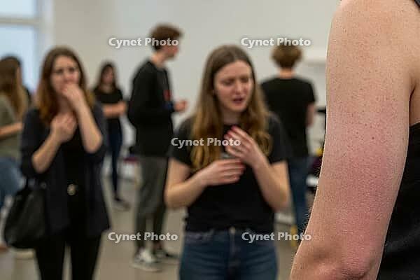 Authentic vocal training and performing arts education in a minimalist studio, young adults engaging in emotional communication exercises, expressive body language and speech practice, an expressive young woman gesturing nervously near her chest during an [IBR125446458]