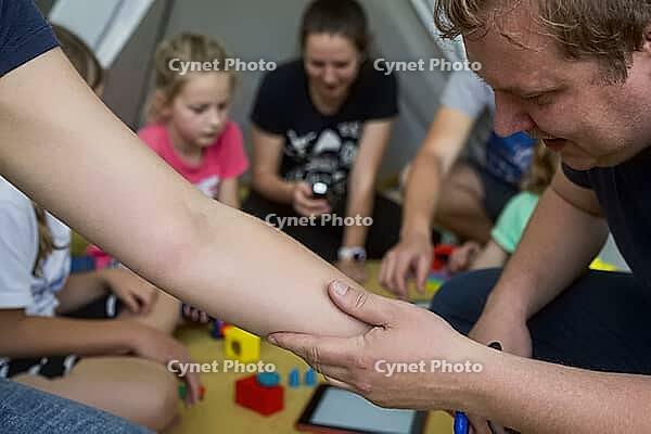 Pediatric care and health examination during child play, a caring hand gently inspects an extended arm for minor injuries or allergic skin reactions, the supportive touch embodies parental vigilance alongside tactile empathy, children and guardians gather [IBR125446479]
