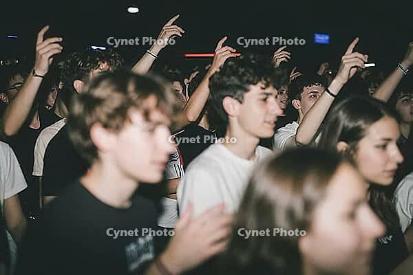 Collective euphoria and youth culture in vibrant nightlife club concerts, enthusiastic teenagers raise arms in unison during live music performance, energetic atmosphere of adolescent escapism and emotional release in dimly lit venue spaces, blurred motio [IBR125446486]