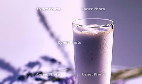 Tall glass holds creamy lavender milkshake. Soft purple lighting enhances calm mood. Blurred lavender sprig adds natural touch, AI generated [IBR125446491]