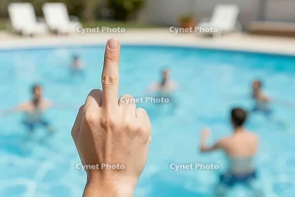 Middle finger hand gesture of rejection against blurred tourists in a swimming pool, showing social isolation and contempt amidst sunny resort leisure, emotional dissonance between collective recreational joy and individual hostility, harsh daylight illum [IBR125446496]