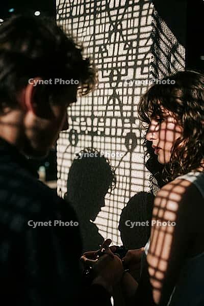 Interpersonal intimacy amidst geometric grid shadows, two lovers standing close in dramatic chiaroscuro illumination, contemplative longing and delicate emotional attachment between young adults, the intricate lattice projection across a textured wall con [IBR125446498]