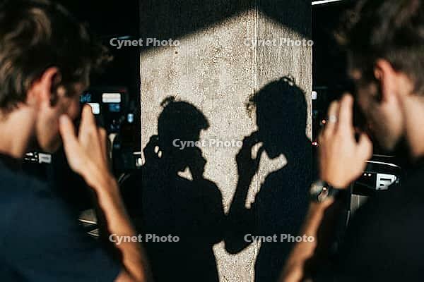 Shadow silhouettes of two young men reflected on a weathered concrete column reveal introspection, emotional vulnerability, psychological tension, urban alienation in subterranean darkness, symmetrical human outlines mirroring identical reflective gesture [IBR125446508]