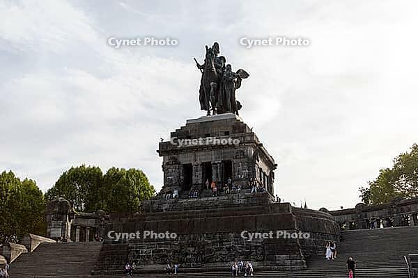 Young people and tourists sit on the steps of the Deutsches Eck tourist attraction at the confluence of the Moselle and Rhine rivers, Koblenz, Germany [IBR125448863]