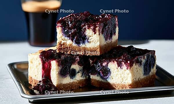 Two stacked blueberry cheesecake slices on metal plate. Dark background with coffee cup behind. Slightly blurred background, AI generated [IBR125448887]