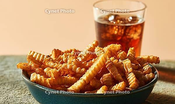 Crispy crinkle-cut french fries in dark bowl. Glass of iced cola beside fries. Warm-toned background. Food close-up, appetizing, casual meal, AI generated [IBR125448894]