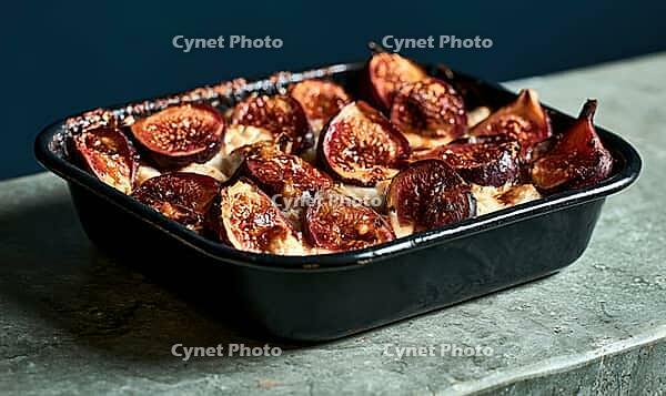 Roasted figs in a black baking dish on stone surface. Warm, caramelized fruit glistens under soft light. Dark background contrasts with rich, AI generated [IBR125448900]