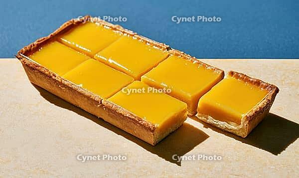 Sweet mango tart sliced into squares. One piece removed, revealing golden crust. Bright yellow filling contrasts with blue background, AI generated [IBR125448901]