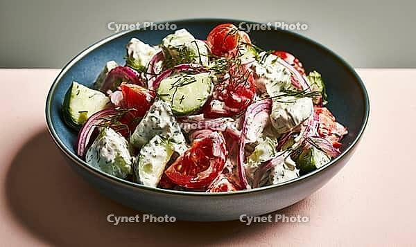Fresh salad with tomatoes, cucumbers, onions, fennel, and yogurt dressing. Served in dark blue ceramic bowl. Vibrant colors, light background, AI generated [IBR125448902]