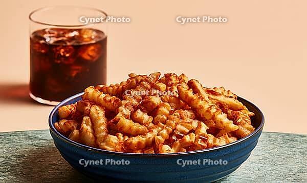 Blue bowl holds crispy, twisted snack sticks. Glass of iced drink sits beside bowl. Warm, neutral-toned background, AI generated [IBR125448905]