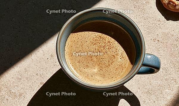Top-down view of coffee in ceramic mug. Sunlight casts shadows on textured surface. Dusting of cocoa powder decorates the coffee, AI generated [IBR125448906]