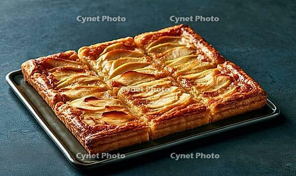 Golden-brown apple tart on dark tray. Crispy pastry with sliced apples. Perfect for dessert or breakfast. Rich, warm tones against dark background, AI generated [IBR125448907]