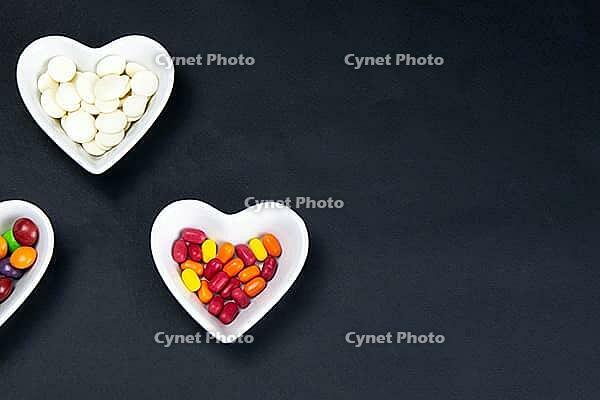 Heart shaped saucer filled with colorful sweets on a black background. Valentine's Day illustration. Top views with clear room [IBR125462057]