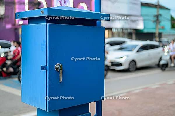 A vibrant blue metal electric or supply box mounted on a pole outdoors, set against a blurred background of urban traffic and street side shops [IBR125462058]
