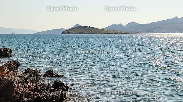 View of the coast at Bitez Bay shows clear blue Aegean sea water with sparkling sunlight reflections and rugged foreground rocks [IBR125462061]