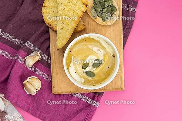 Pea soup with pumpkin seeds, next to greens and pumpkin with garlic stand on a purple towel. Top views with clear room [IBR125462072]