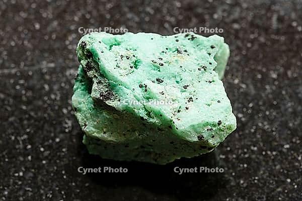Specimen of mineral from geological collection - rough chrysocolla rock with black libethenite crystals close-up on black granite background from Alaverdi, Armenia [IBR125462094]