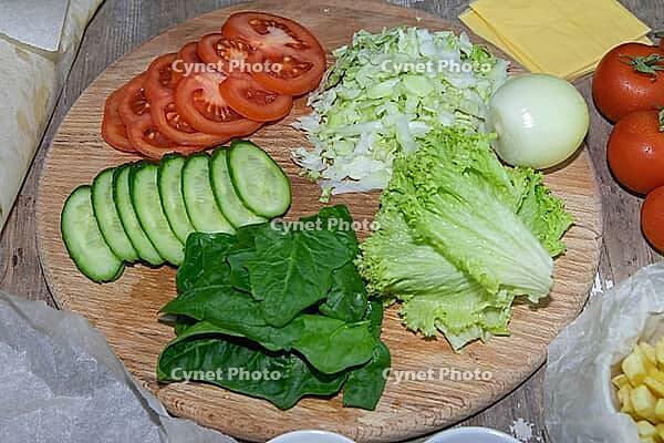 Preparation for the preparation of hamburgers. On a wooden board are lettuce leaves chopped: tomatoes, cucumbers, onions, sweets and sauces [IBR125462104]